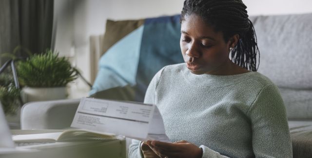 Woman sat by sofa reading paper utility bill