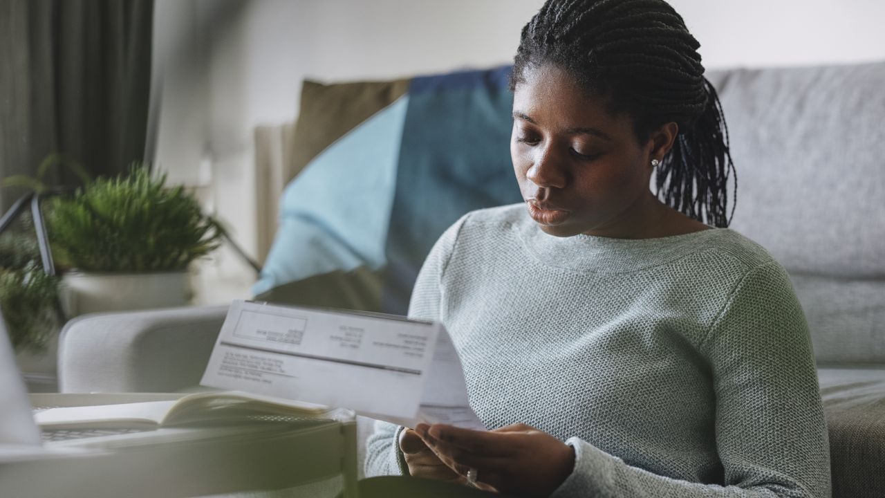 Woman sat by sofa reading paper utility bill