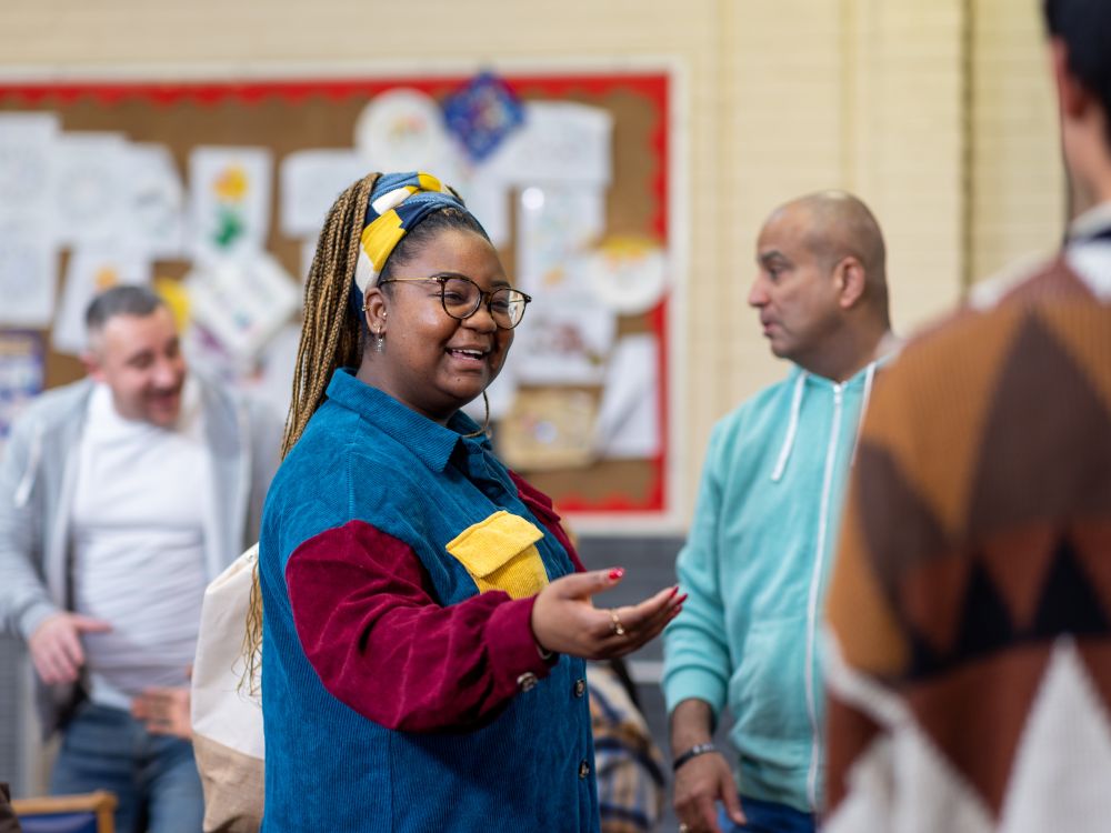 Woman holding out her hand welcoming someone to a group of people stood chatting in the background