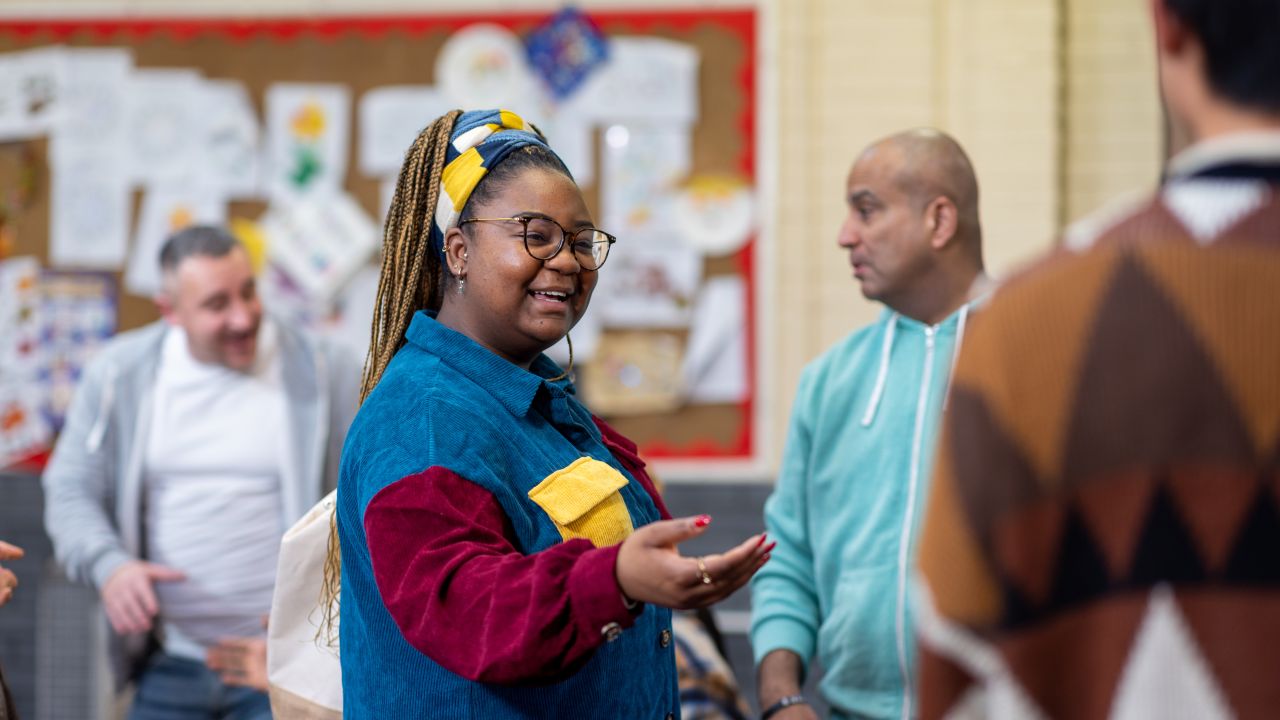 Woman holding out her hand welcoming someone to a group of people stood chatting in the background