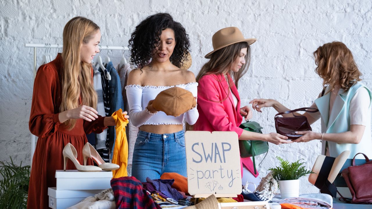 Four women looking at clothes and bags by a sign that reads "Swap party"