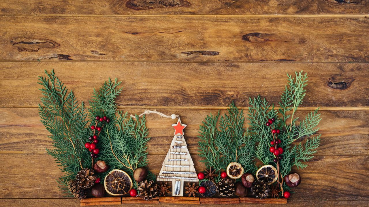 Christmas plastic free: decorations over a wooden background, including pine cones, pine leaves, dried orange and a miniature wooden Christmas tree