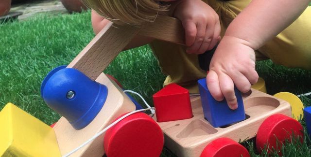 Toddler playing with colourful wooden toy crane on wheels