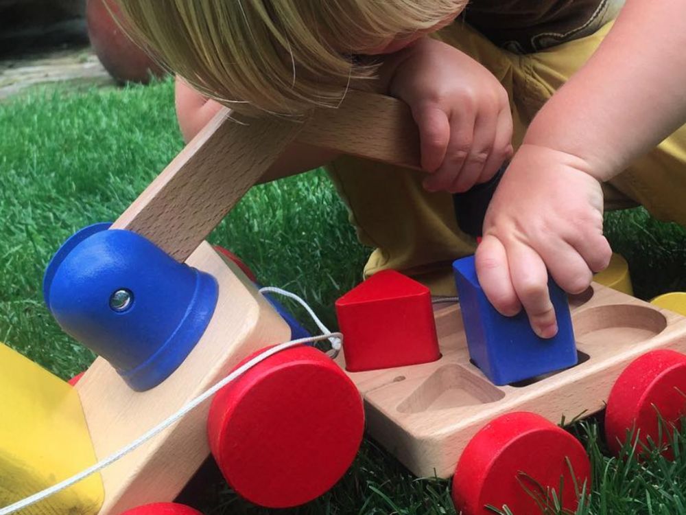 Toddler playing with colourful wooden toy crane on wheels