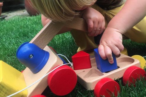 Toddler playing with colourful wooden toy crane on wheels