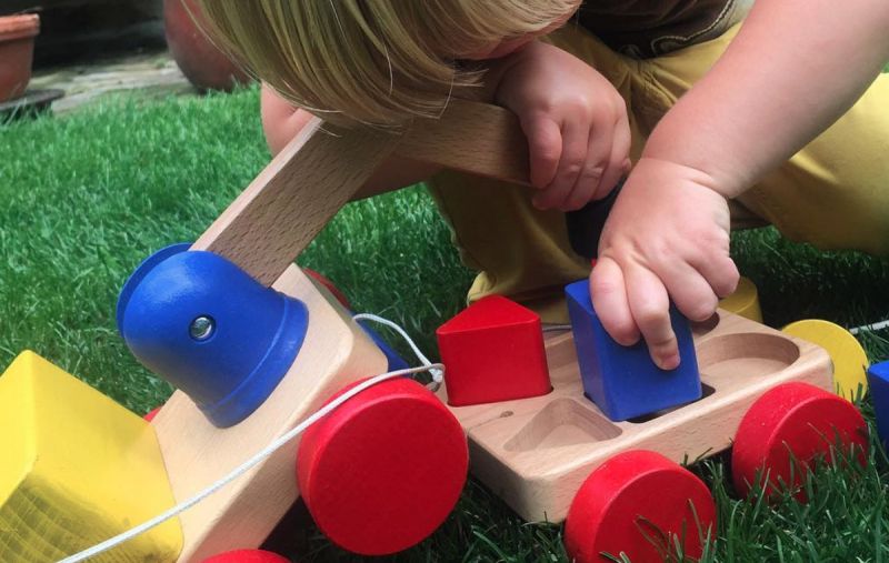 Toddler playing with colourful wooden toy crane on wheels