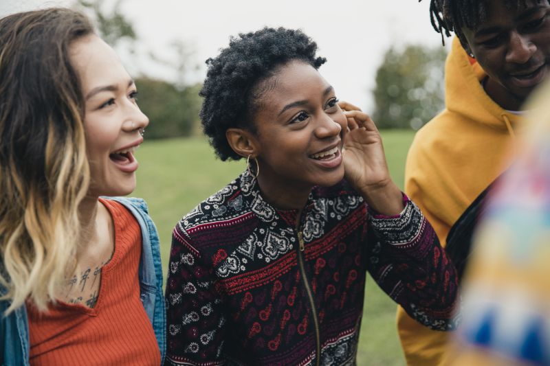 Three young people talking and smiling in a park
