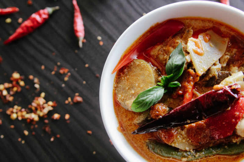 Vegan vegetable stew with dumplings in a dish on a table with red chillis scattered around.