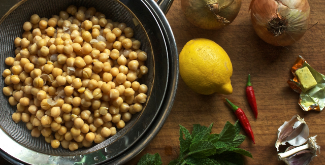 Chickpeas in sieve in bowl next to lemon, onions, chillies mint and stock cube