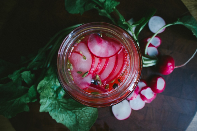 Beautiful sliced picked radishes in a fermenting jar, with extra radish on chopping board