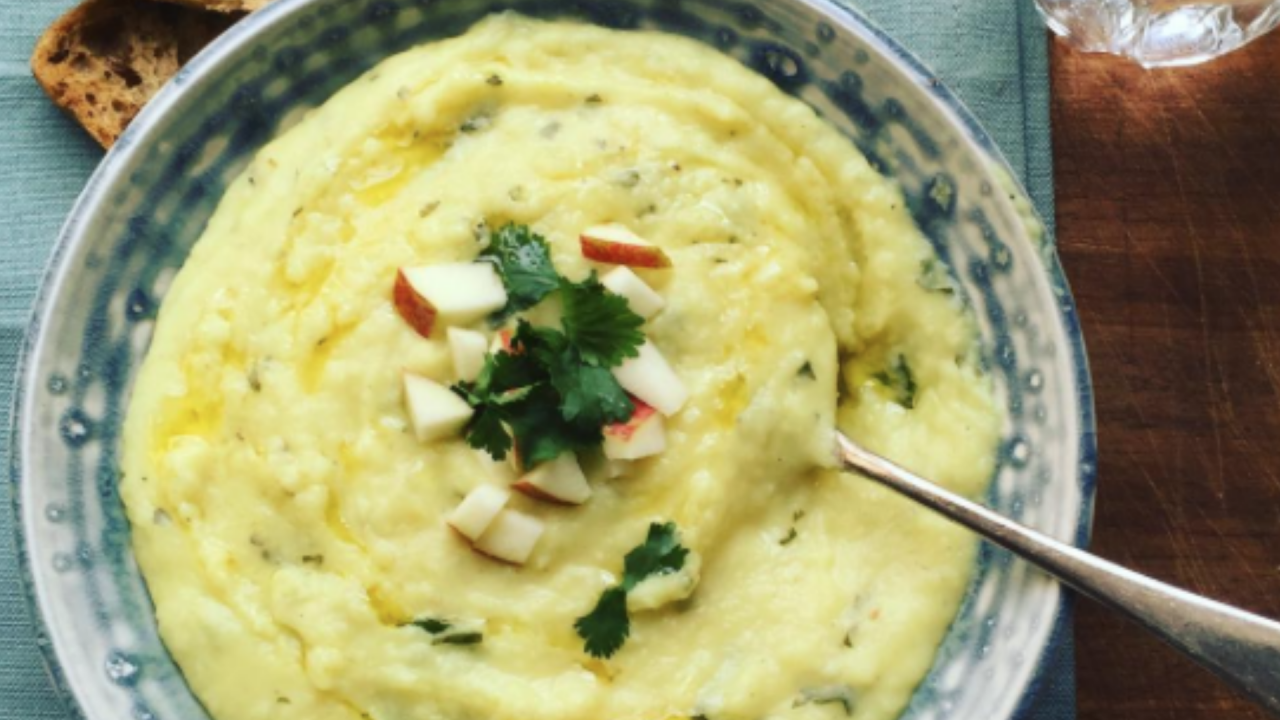 A bowl of ginger and parsnip soup with a garnish of of apple, parsley and ginger