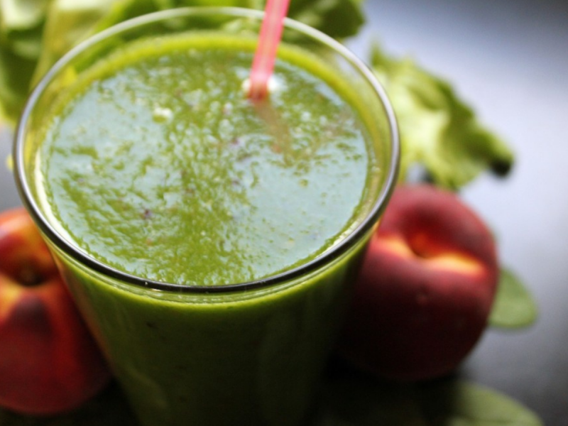 Green vegetable smoothie in glass with fruit next to it