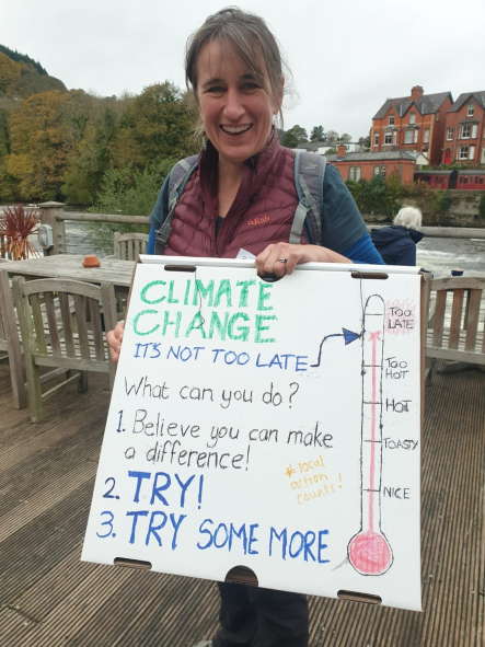 Robyn stands by a river, holding a placard about climate change.